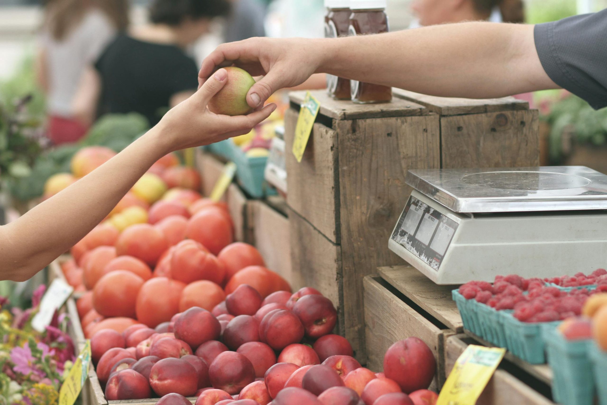 A fruit stand owner passing a customer an apple.