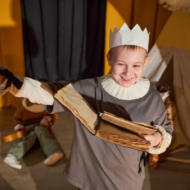4-h youth member with crown, grey long sleeve, and white crown, reading a play at a talent show.