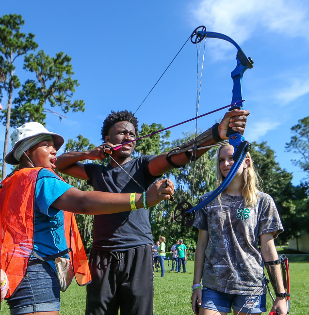 4-H youth participating in an outdoor archery activity with adult guidance.
