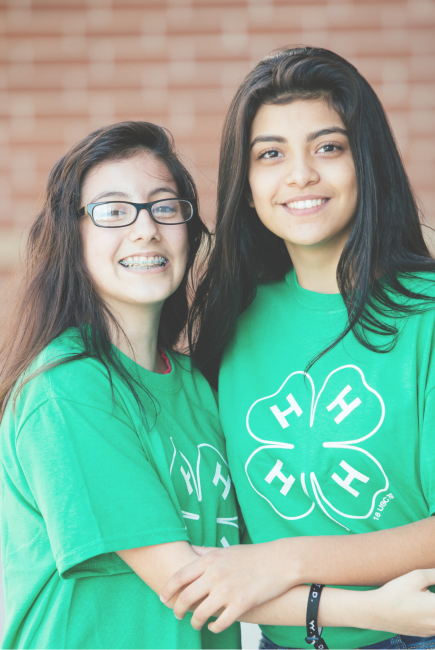 Two 4-H members wearing green 4-H shirts stand together and pose for a photo.