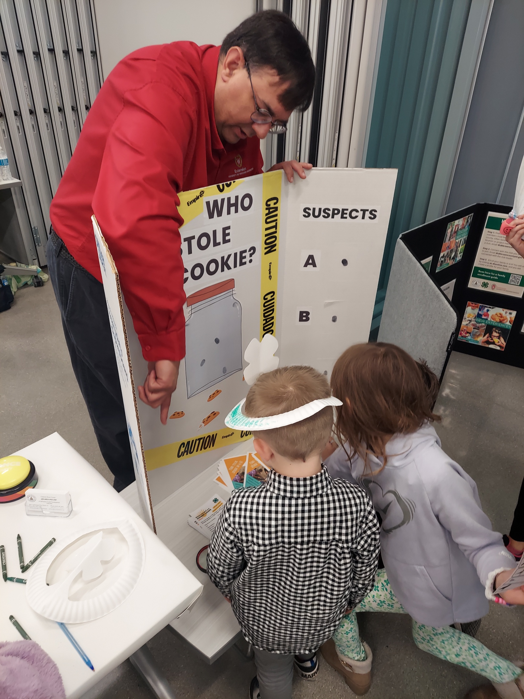Children participate in a hands-on 4-H activity while an educator explains a crime-solving themed learning display.