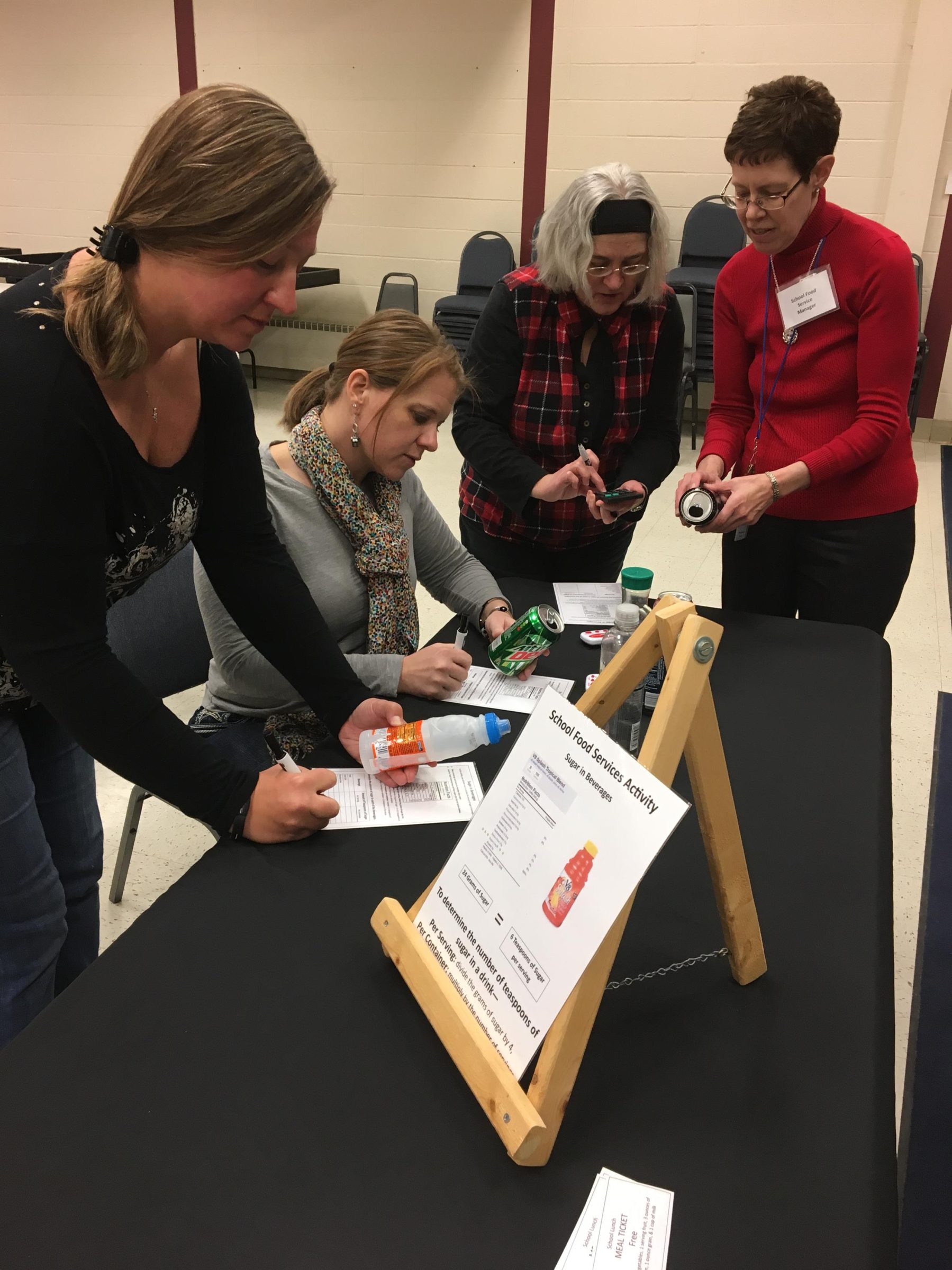 Image of a group of women at a table looking a nutritional labels on the back of the soda cans