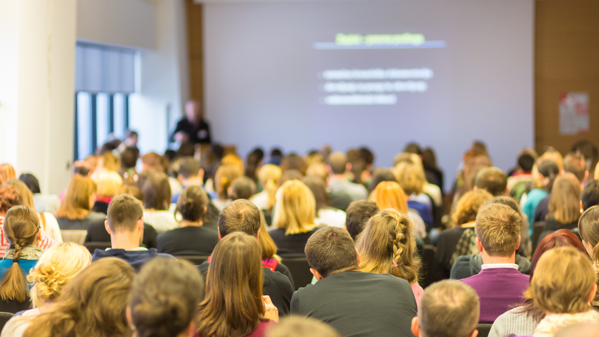 Image of various people sitting in a conference room viewing presentation