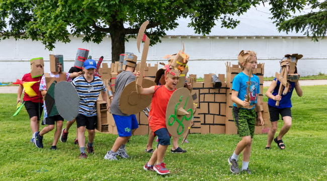Children in cardboard made armor and tools running towards opponent